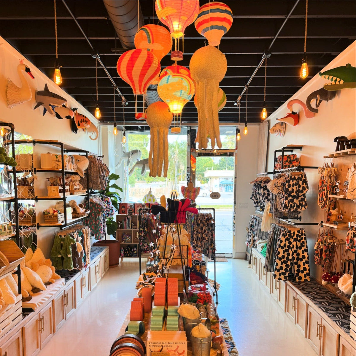 Inside the Best Day Ever Kids showroom: racks of printed clothes, toys on shelves and colorful paper lanterns overhead