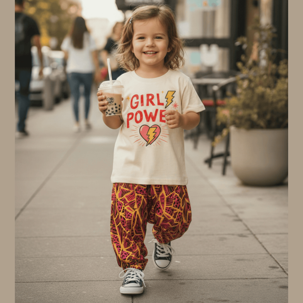 Smiling kid in the Girl Power Graphic Tee and Neon Jungle Hammer Pants walking down a sidewalk