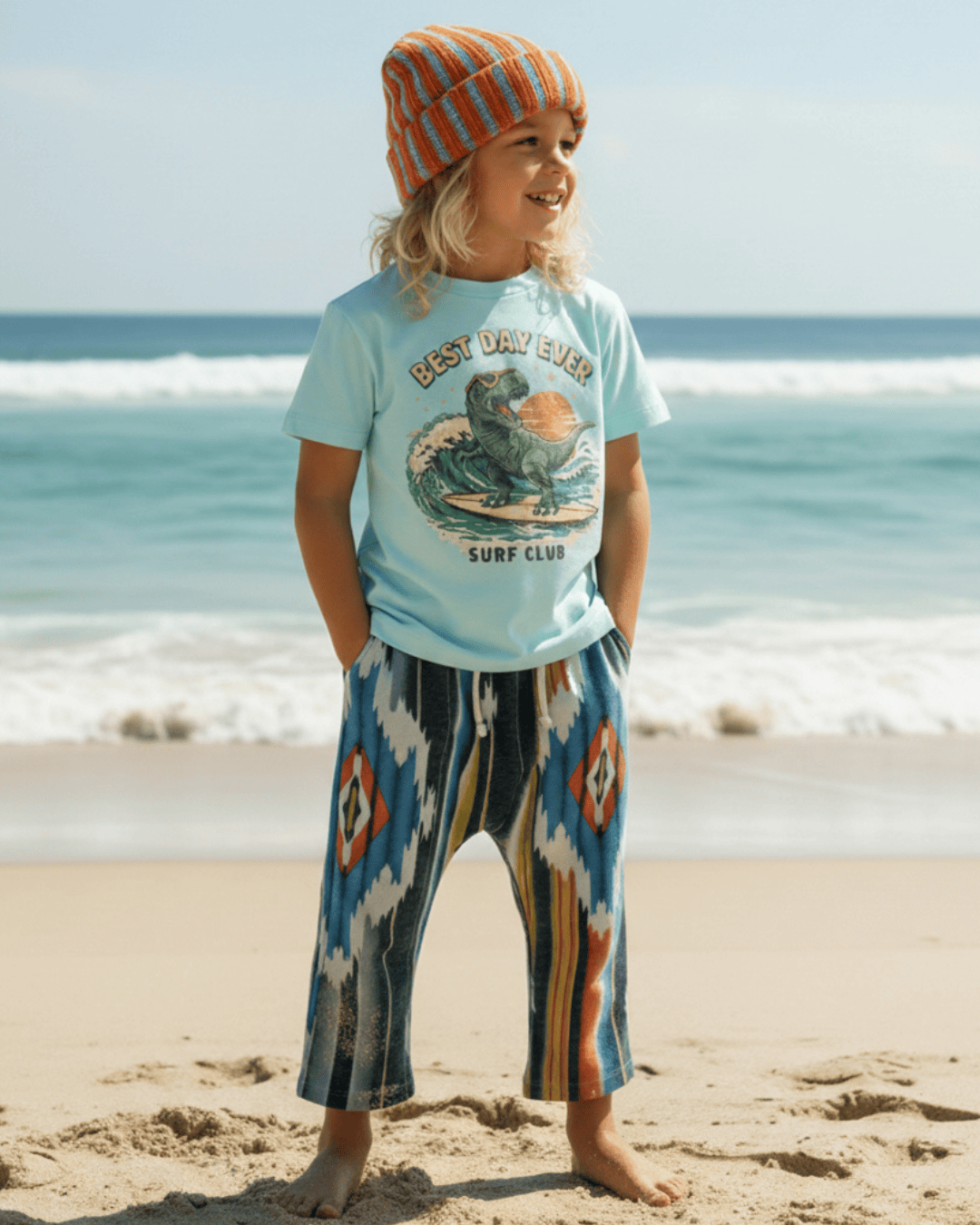Kid in a beanie on a beach wearing the Surf Club Tee with Southwest print pants