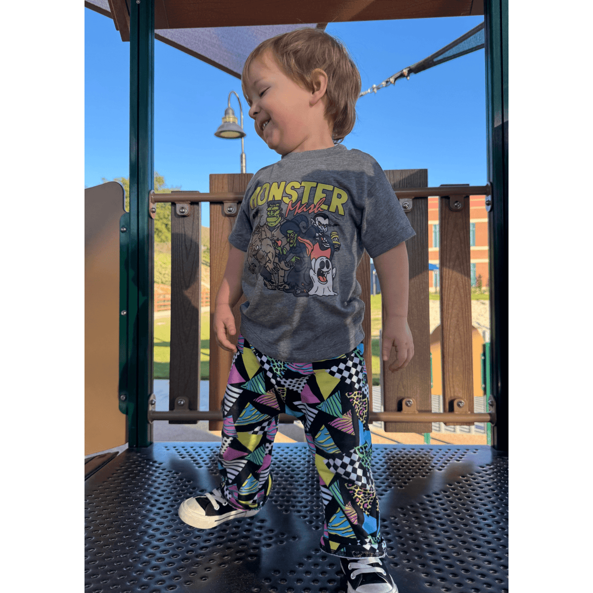 Toddler on a playground wearing the Monster Mash Tee with bright print pants
