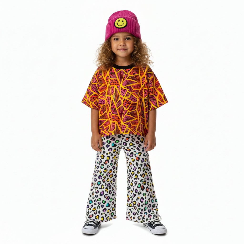 Kid in a pink smiley beanie wearing the Neon Jungle Oversized Tee with rainbow leopard wide-leg pants