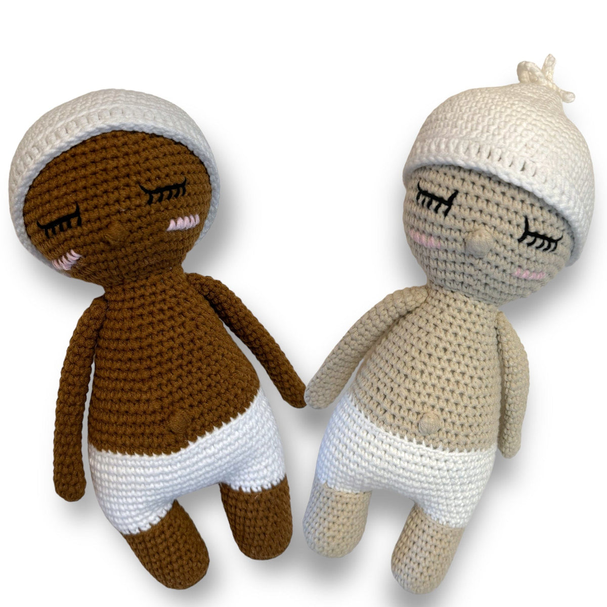 Two sleeping hand-crocheted baby dolls in diapers and knit hats, in two skin tones