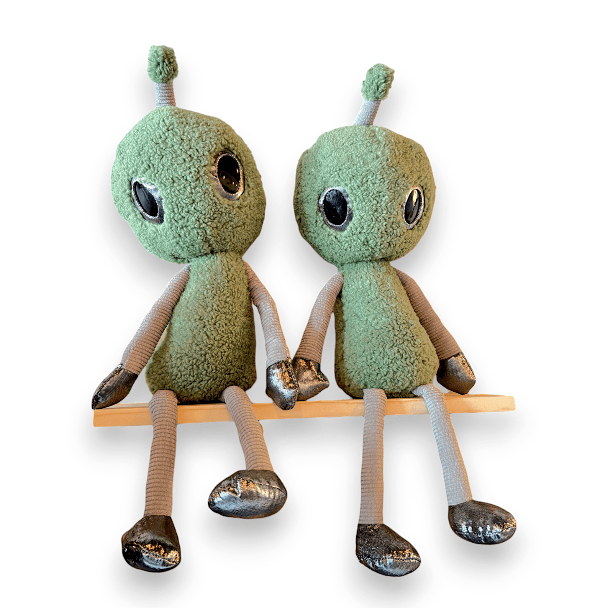 Two green Cosmo the Friendly Alien plush toys sitting side by side on a shelf