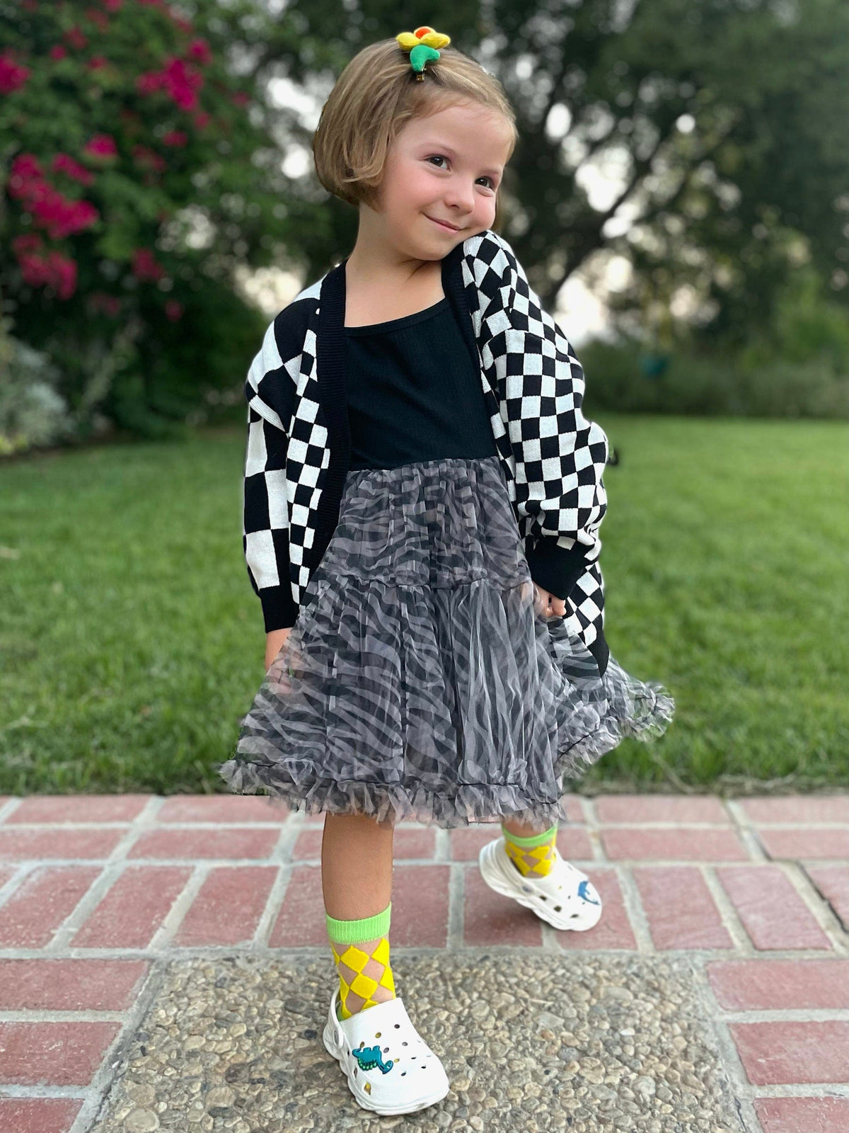 Kid in a checkered cardigan and gray tulle skirt wearing Happy Harlequin socks with sneakers