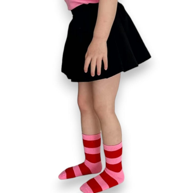Kid in a black skirt wearing pink-and-red Happy Stripe socks pulled up high