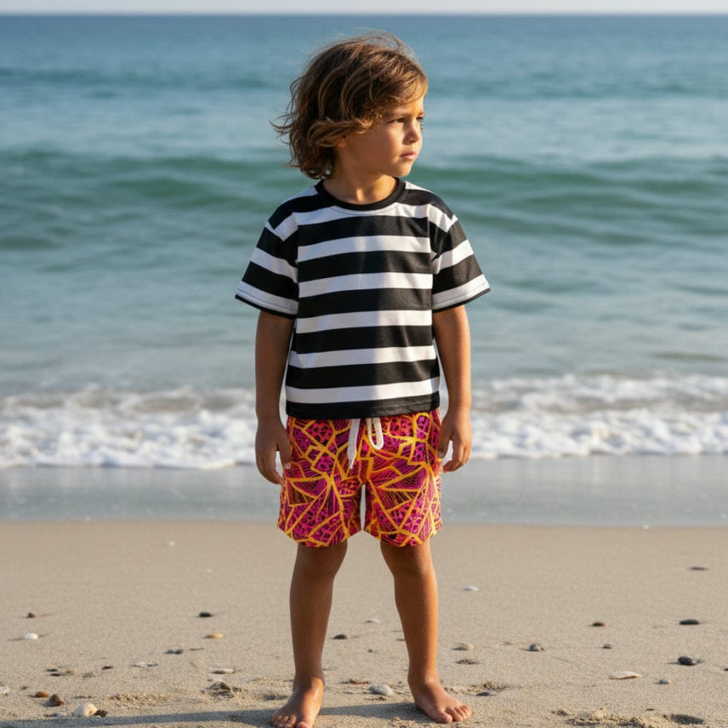 Kid in a striped tee on a beach wearing Neon Jungle Swim Trunks