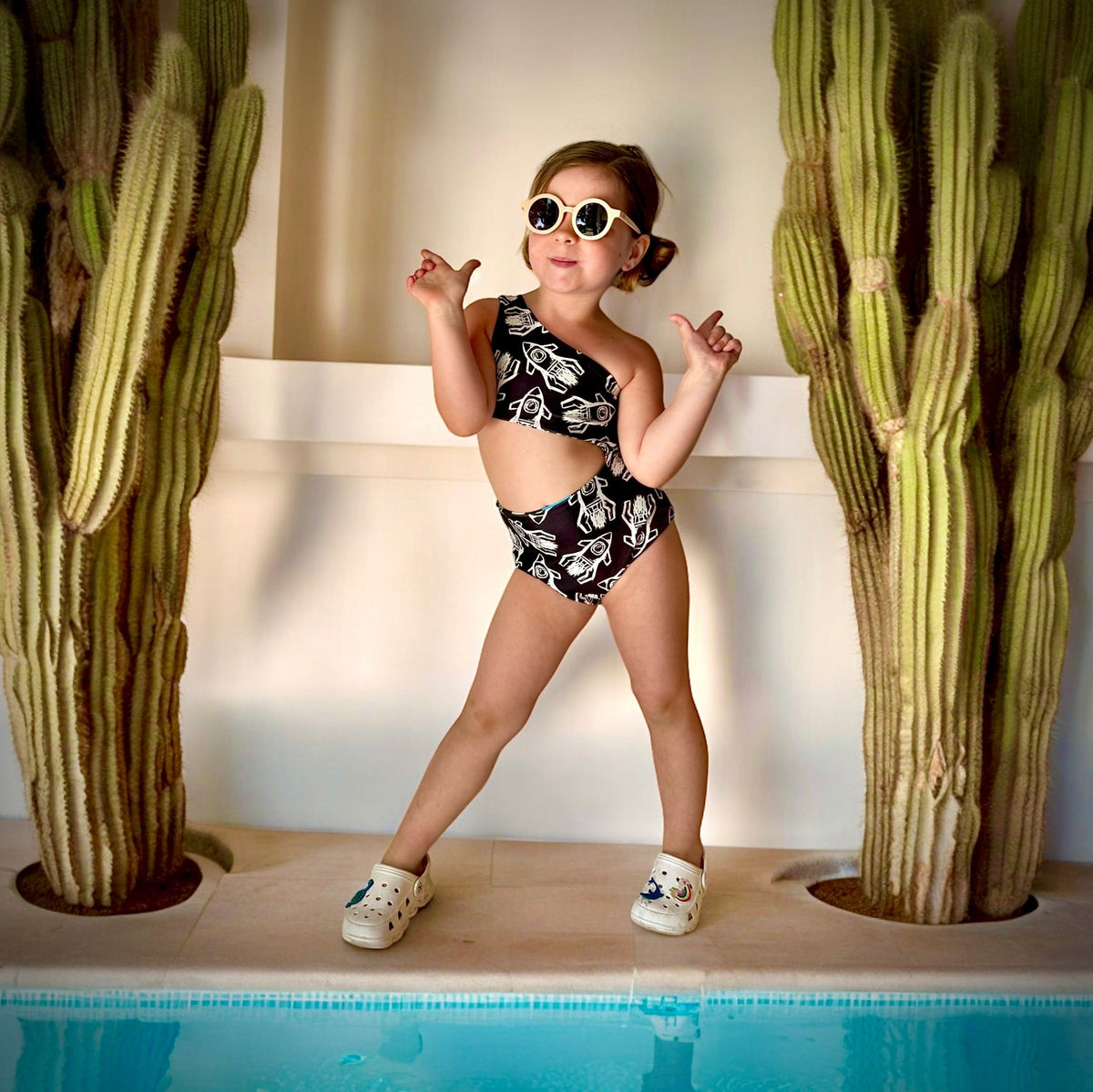 Kid in sunglasses posing by cacti in the Rad Rockets reversible swimsuit