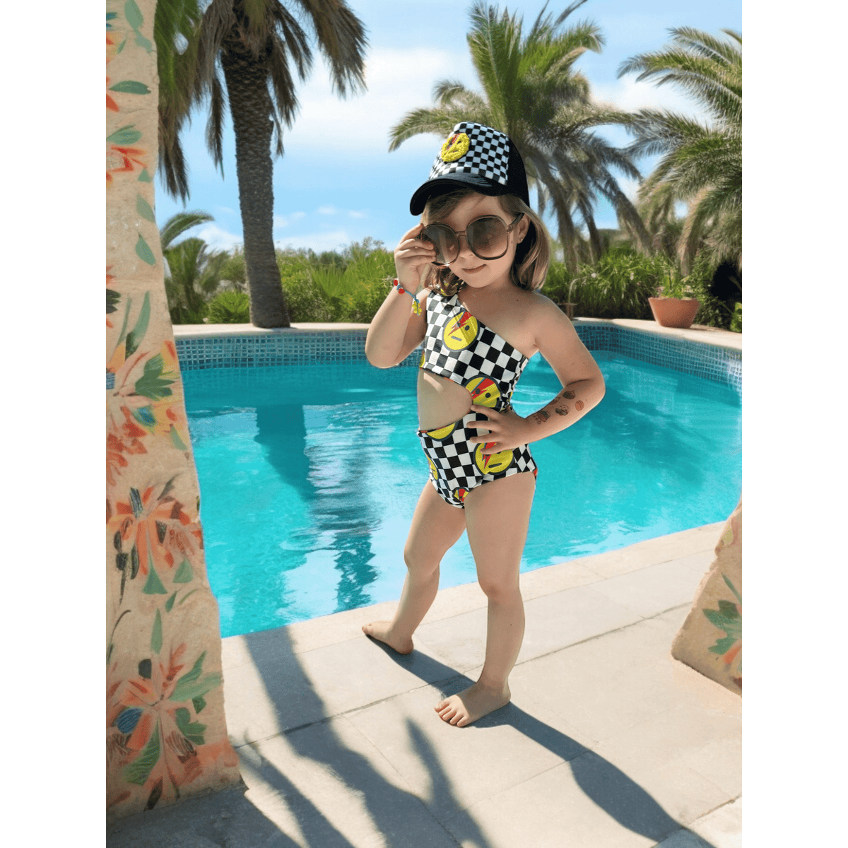 Kid in a matching checkered cap wearing the Star Man reversible swimsuit by a pool