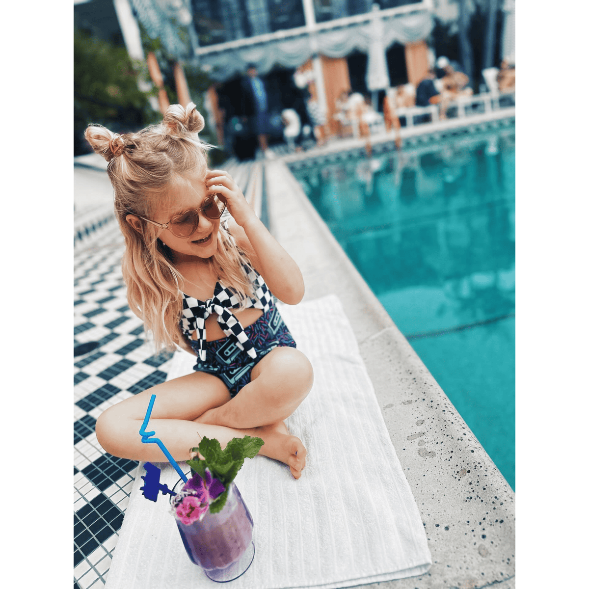 Kid in the Rewind Swimsuit and heart sunglasses sitting poolside