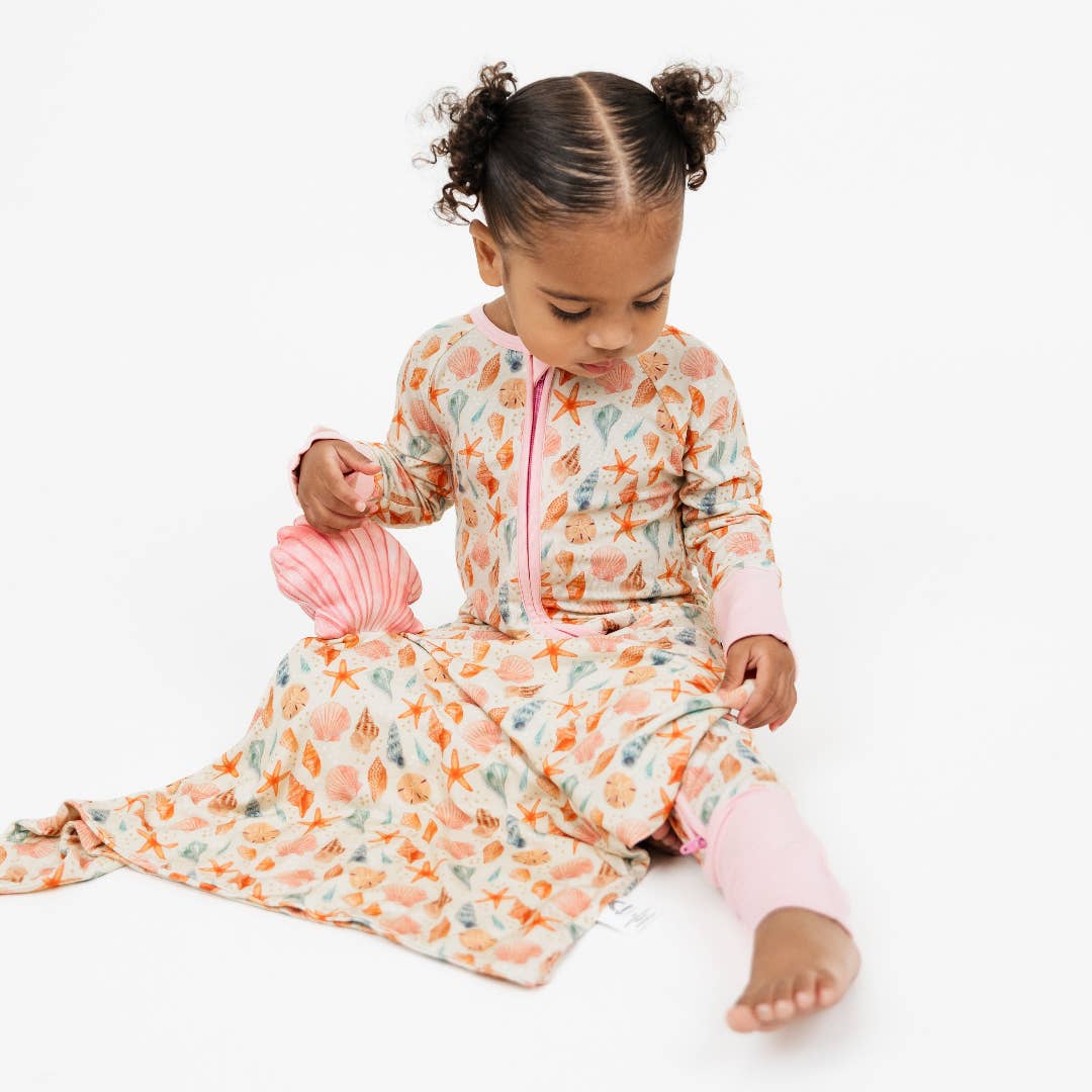 Toddler in seashell print pajamas holding the seashell lovey