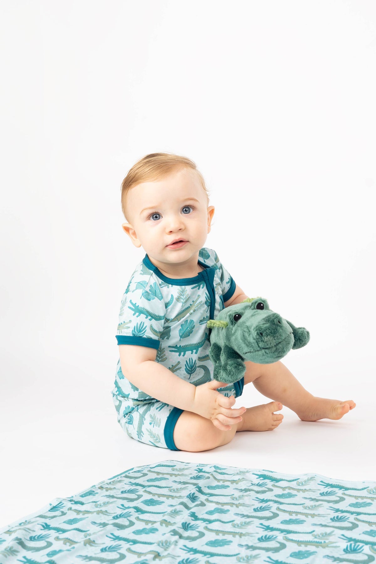 Baby in alligator print pajamas holding Andy the alligator