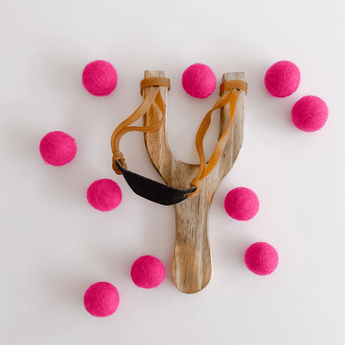 Wooden slingshot surrounded by pink felt balls