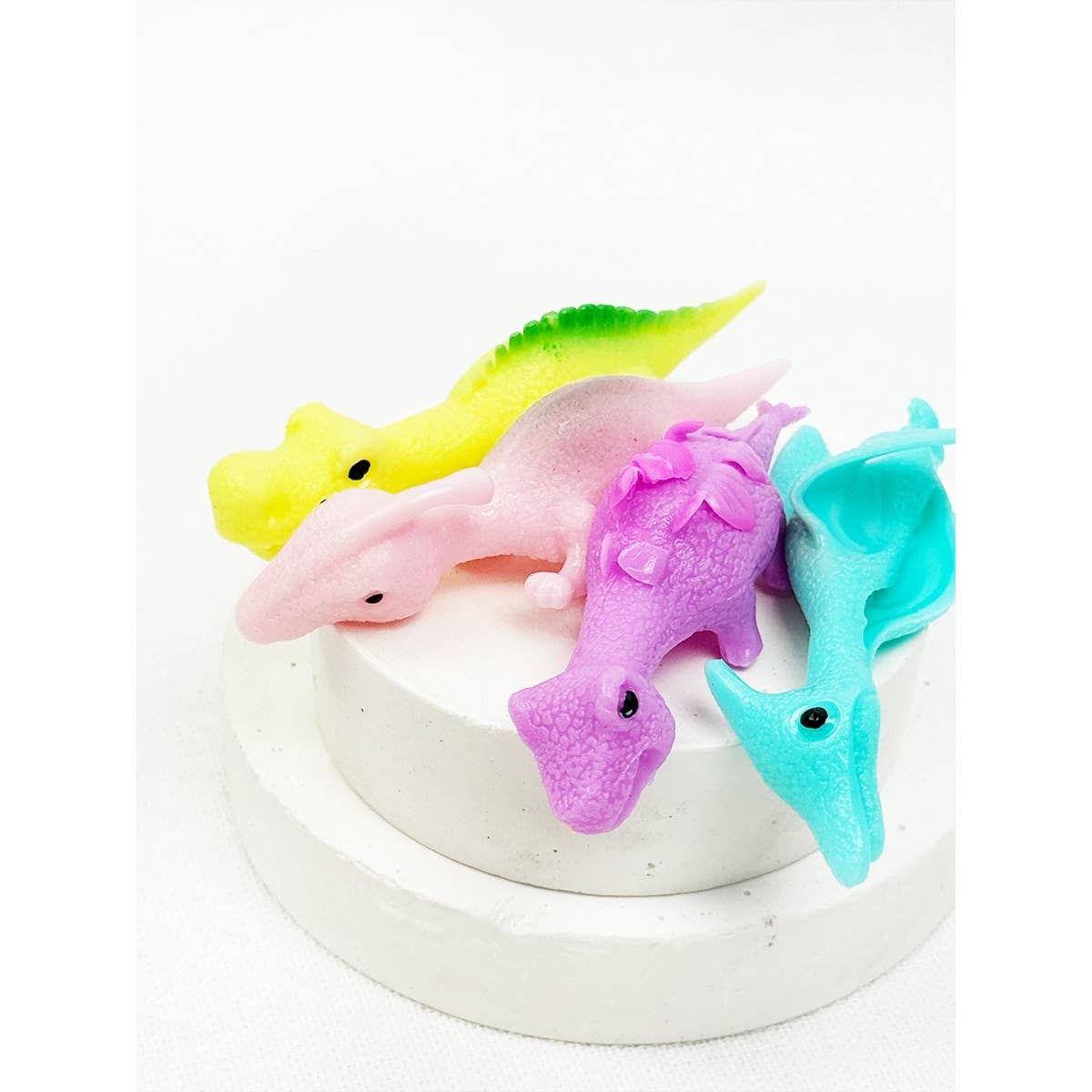 Four stretchy slingshot dinosaurs in yellow, pink, purple and teal
