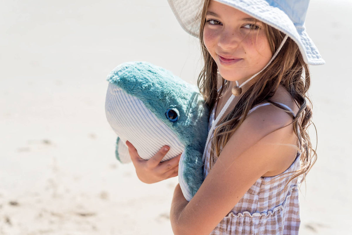 Smiling girl in a sun hat hugging Hurley the Whale on the beach